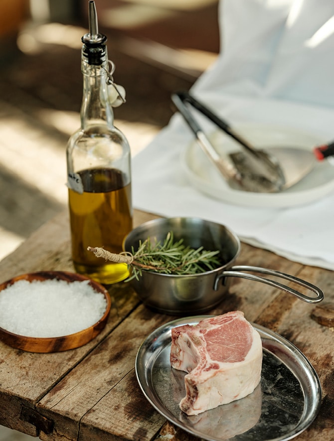 Rosmarin, Meersalz, Öl und ein Wollschweinsteak zum Grillen hergerichtet.